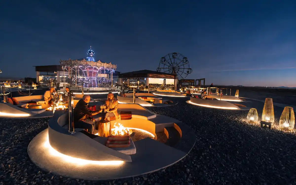 Parejas descansando en un espacio al aire libre con fogatas, luces cálidas y juegos de fondo cerca del Salar de Uyuni.