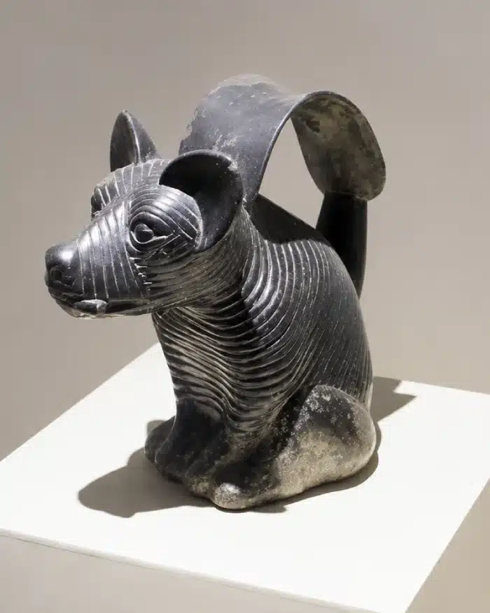 Cerámica con forma de perro peruano sin pelo exhibida sobre un pedestal, con cuerpo oscuro y detalles decorativos
