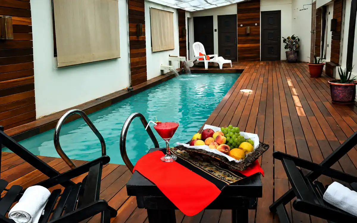 Piscina del hotel Jardines de Uyuni con deck de madera, sillas de descanso, frutas y bebida refrescante.