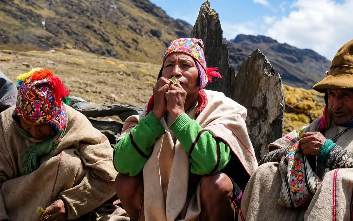 Adultos andinos realizando una ofrenda con hojas de coca en un paisaje de montaña