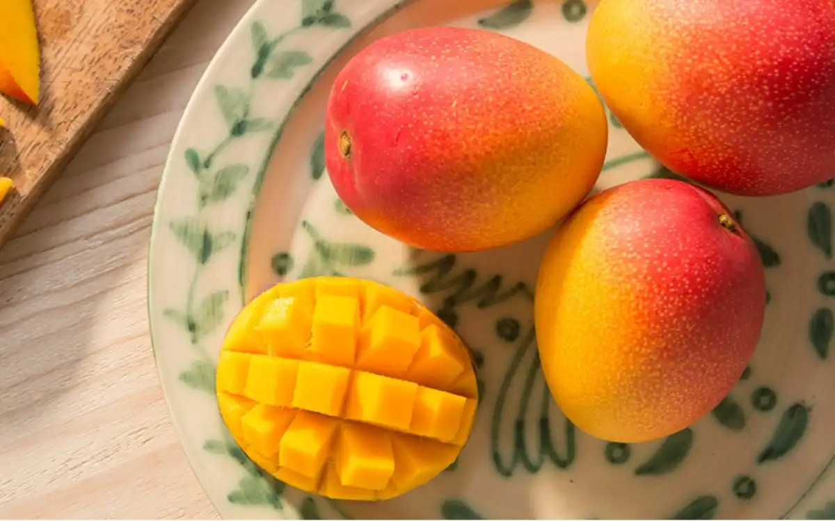 Mangos enteros y mango cortado en cubos sobre un plato