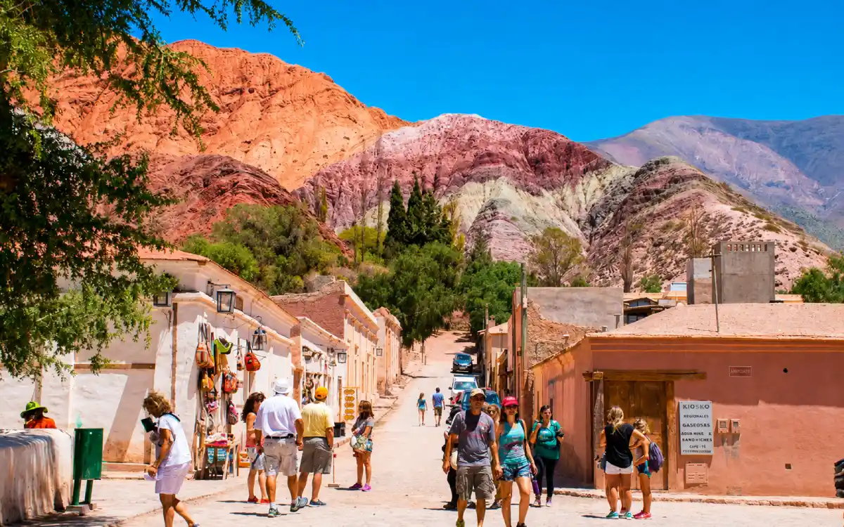 Turistas caminando en un pueblo de Jujuy con montañas de siete colores al fondo