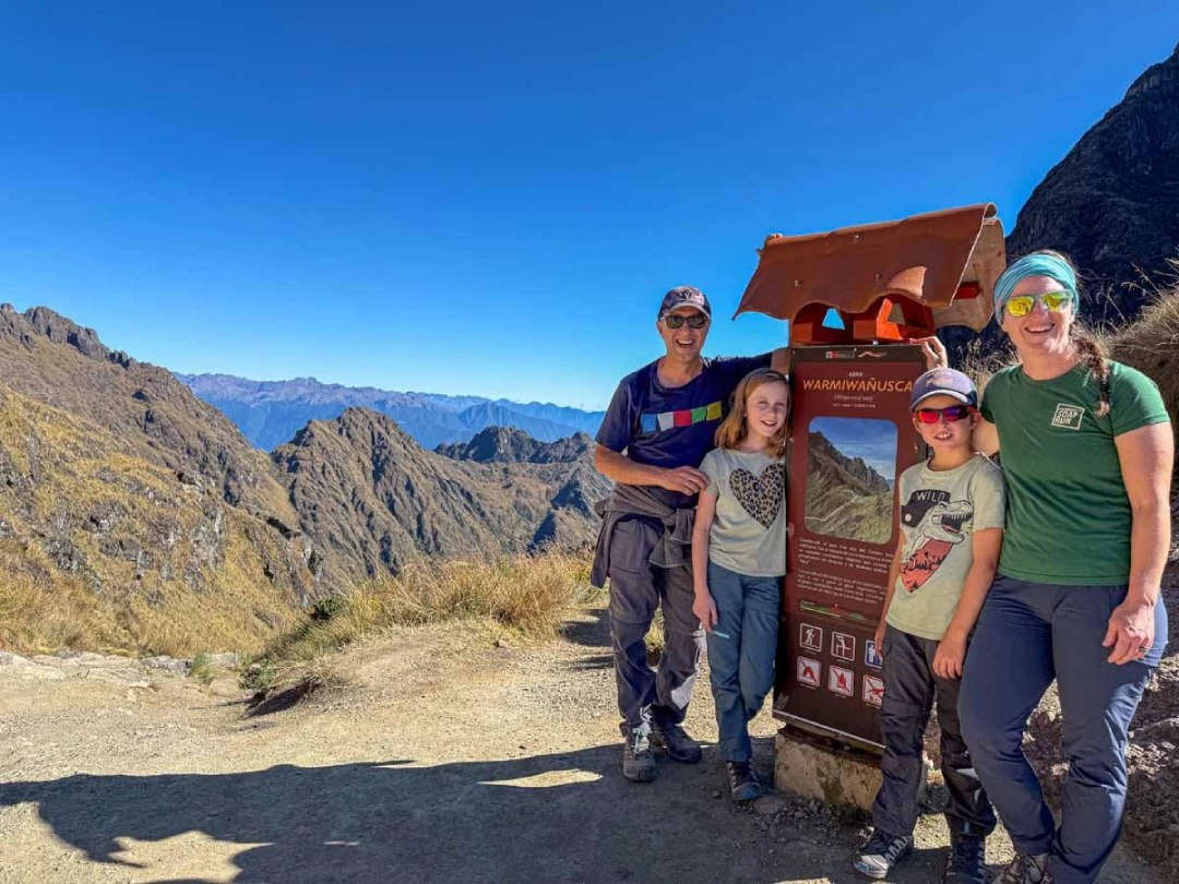Family of hikers poses at Warmi Wañusca, the highest pass on the Classic Inca Trail, surrounded by Andean mountains near Cusco.