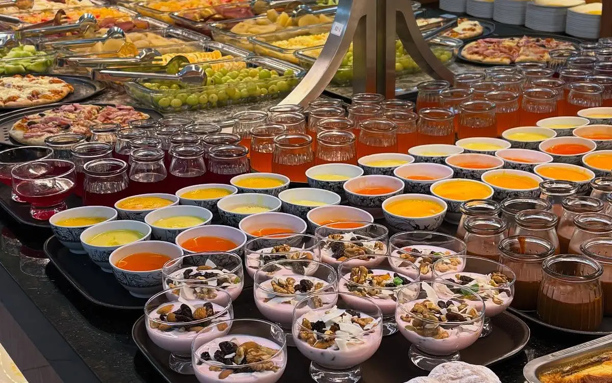 El buffet reúne yogures, jugos, panecillos, frutas y platos preparados, organizados para facilitar el servicio de los huéspedes.