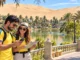 Dos viajeros disfrutan de su visita a Huacachina mientras revisan su ruta frente al paisaje más representativo del oasis.
