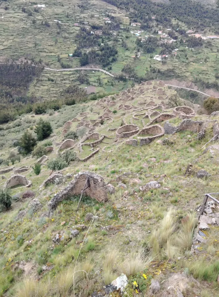 Panoramic view of Ancasmarca’s circular stone structures spread across an Andean hillside in the Cusco region of Peru. From the upper areas of Ancasmarca, visitors can see numerous circular enclosures spread across the slope within a rural landscape of fields, roads and Andean mountains.