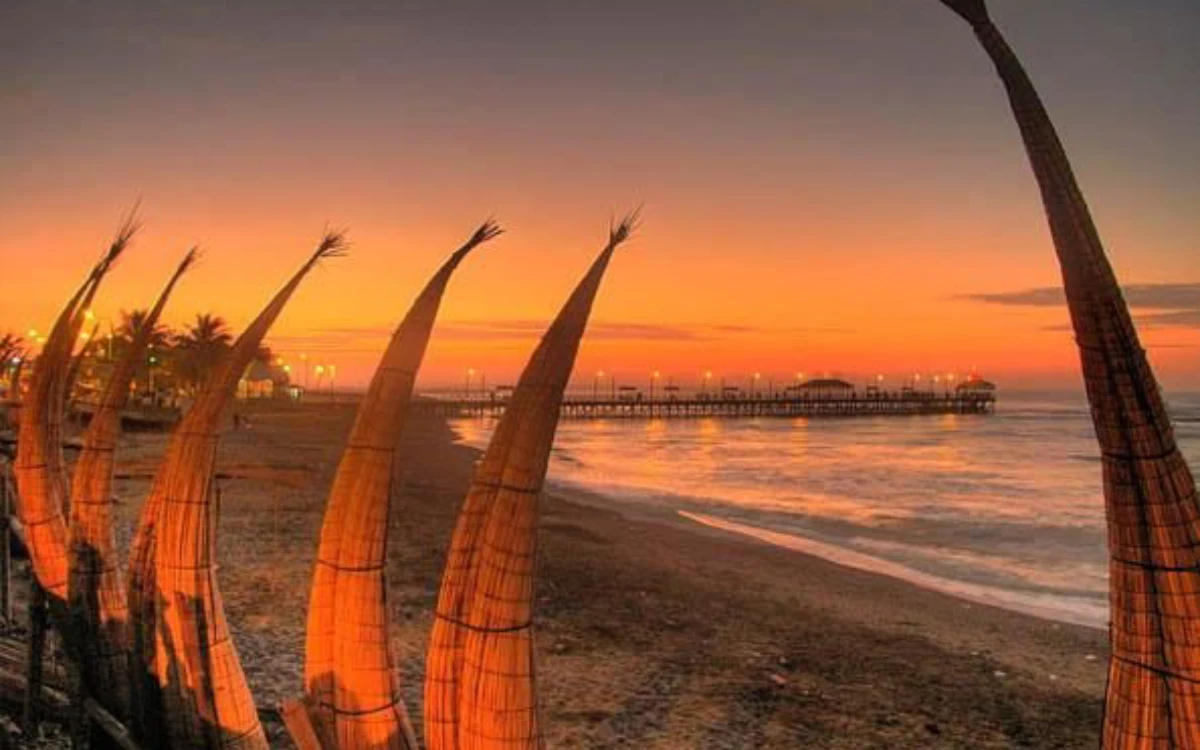 Caballitos de totora en la playa de Huanchaco durante el atardecer con un muelle