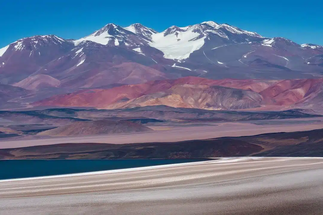 Monte Pissis with snow-covered peaks and volcanic slopes rising above a high-altitude lagoon in the Argentine Andes.