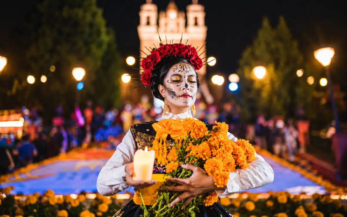 Mujer con maquillaje de Catrina sostiene flores de cempasúchil y una vela