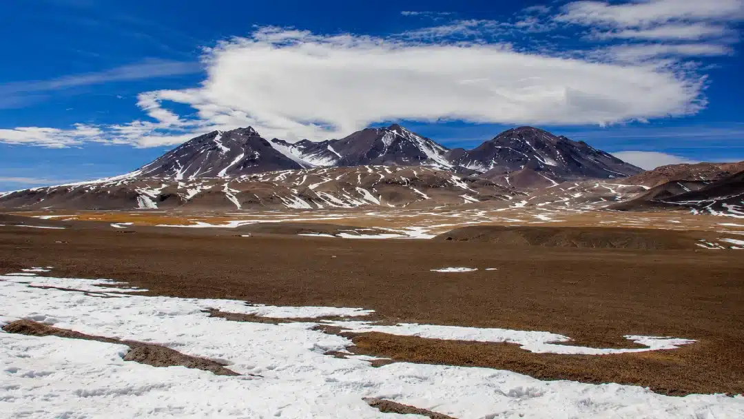 Nevado Tres Cruces with partially snow-covered peaks and broad arid high-altitude plains beneath a blue sky in the Andes.
