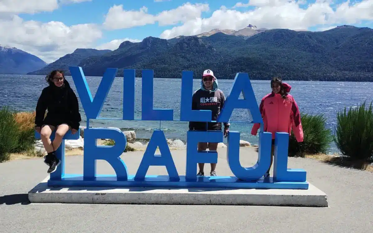 Viajeros junto al cartel de Villa Traful con el Lago Traful y las montañas al fondo