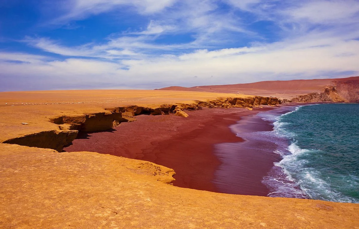 Playa Roja in the Paracas National Reserve, with reddish sand, desert cliffs and Pacific Ocean waves along the coast of Ica, Peru.