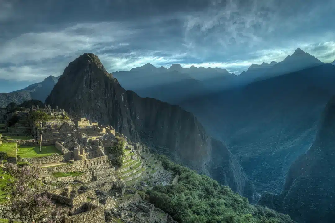 Machu Picchu during the rainy season, with Inca terraces, Huayna Picchu and surrounding mountains covered by clouds and soft light.