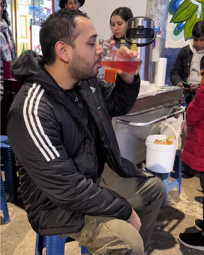 Visitante tomando un vaso de emoliente tradicional junto a una carreta en Cusco