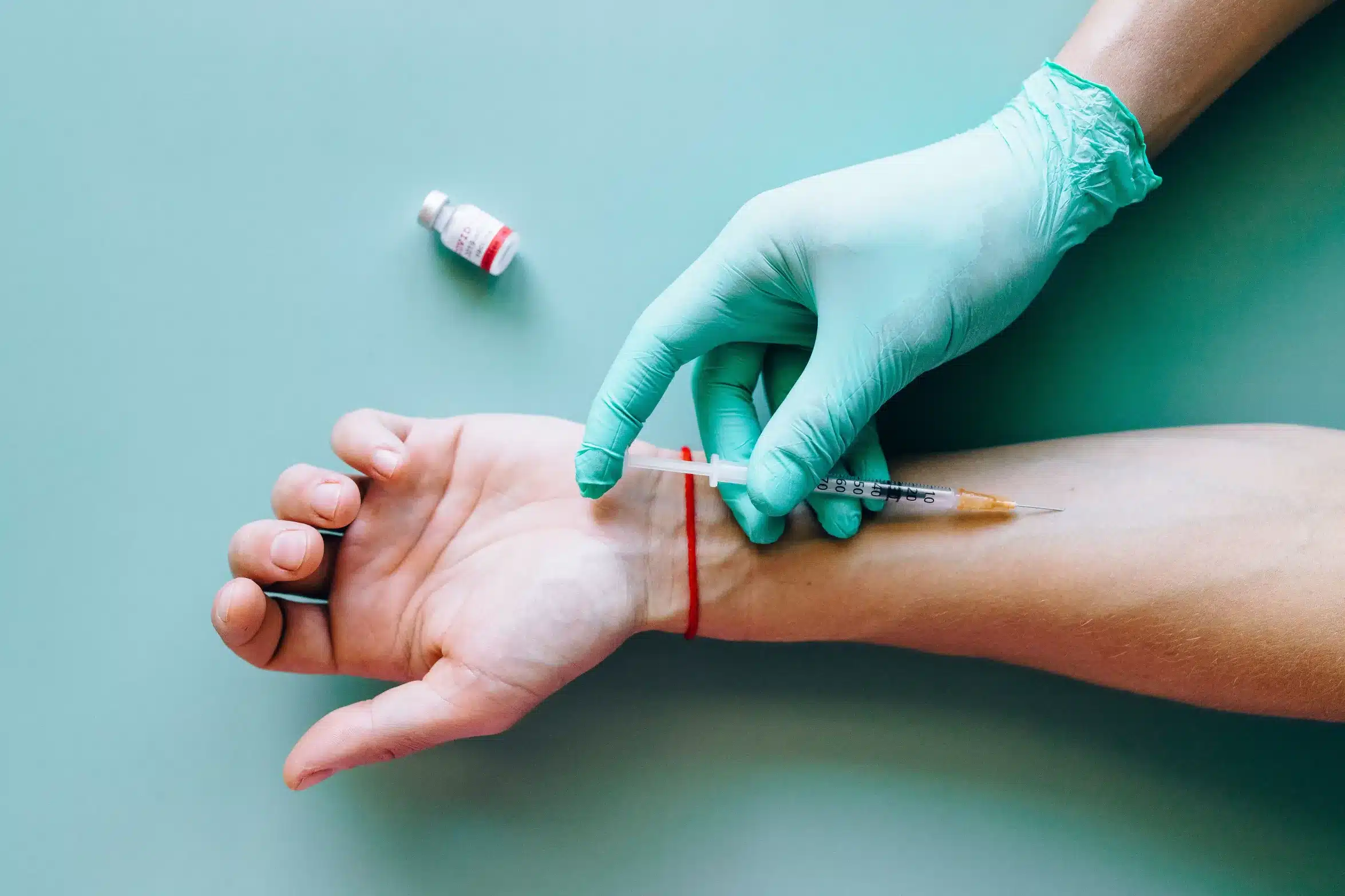 Healthcare professional wearing gloves administers an injection into a person’s arm as part of a vaccination procedure.