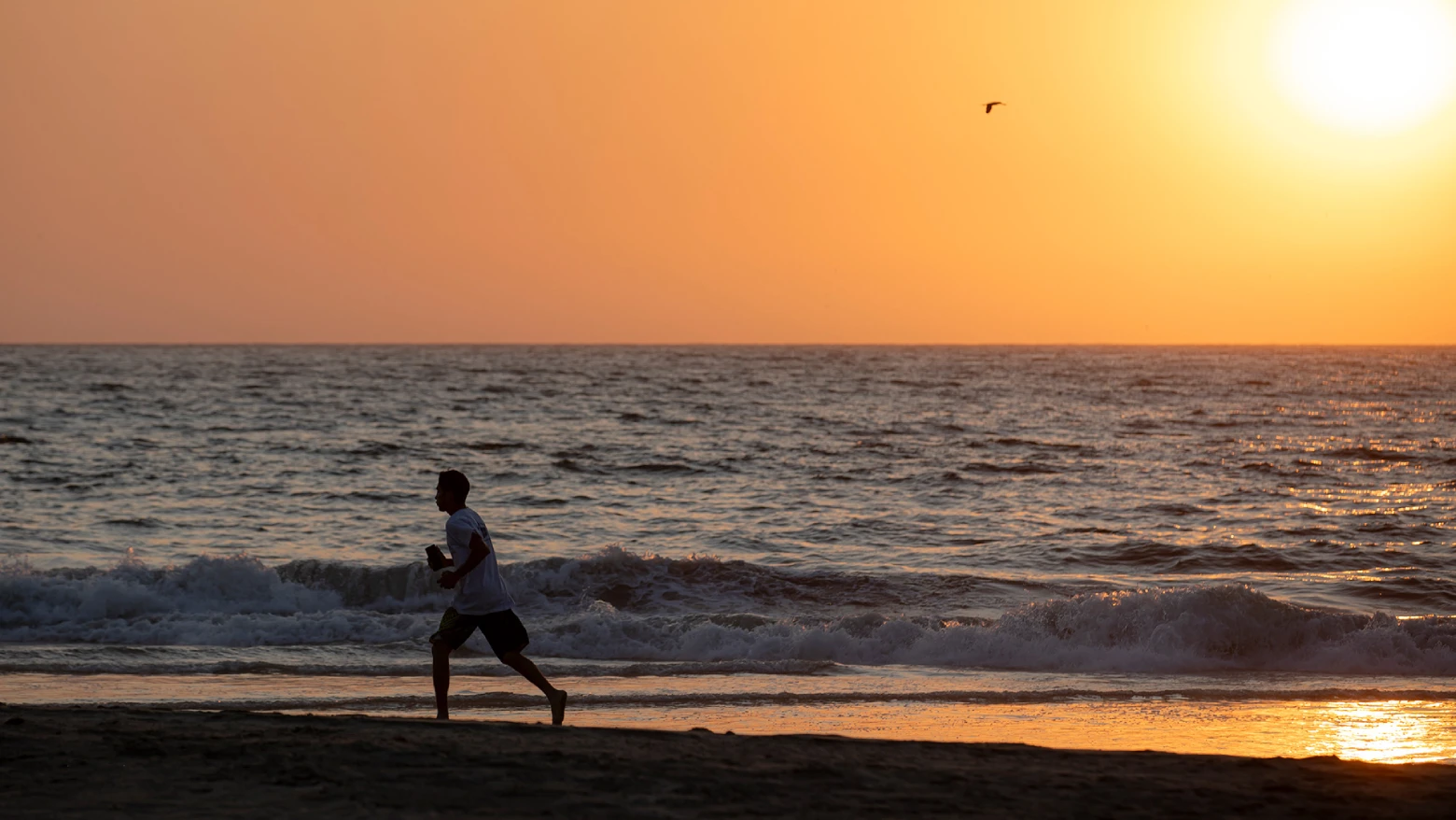 Traveler runs along Vichayito Beach at sunset, with Pacific Ocean waves and an orange sky on Peru’s northern coast.