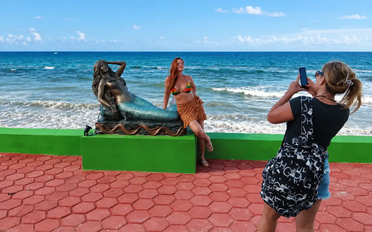 Turista posando junto a una escultura de sirena en el Paseo de las Sirenas de Isla Mujeres